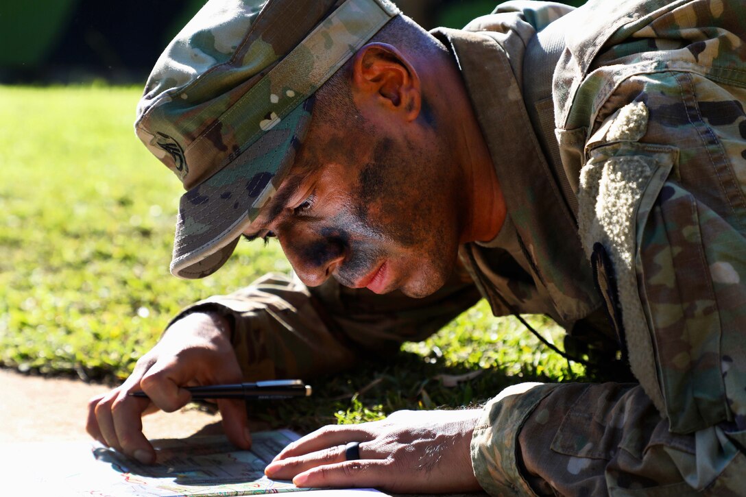 A soldier plots coordinates on a map using a protractor.