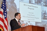 Chris Hall speaks from behind a lectern with a presentation on the screen behind him.