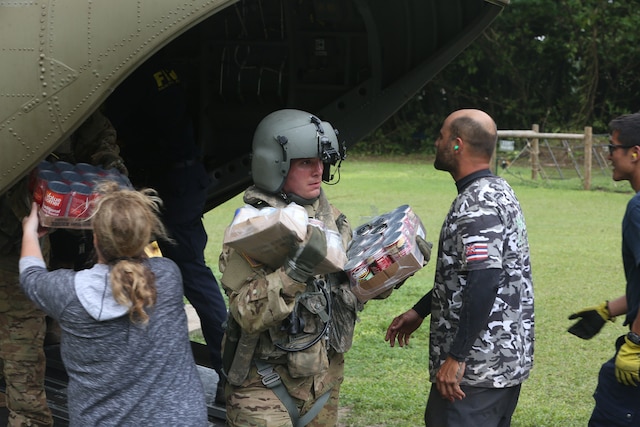 Soldiers hands boxes of food to civilians out the back of a helicopter.  