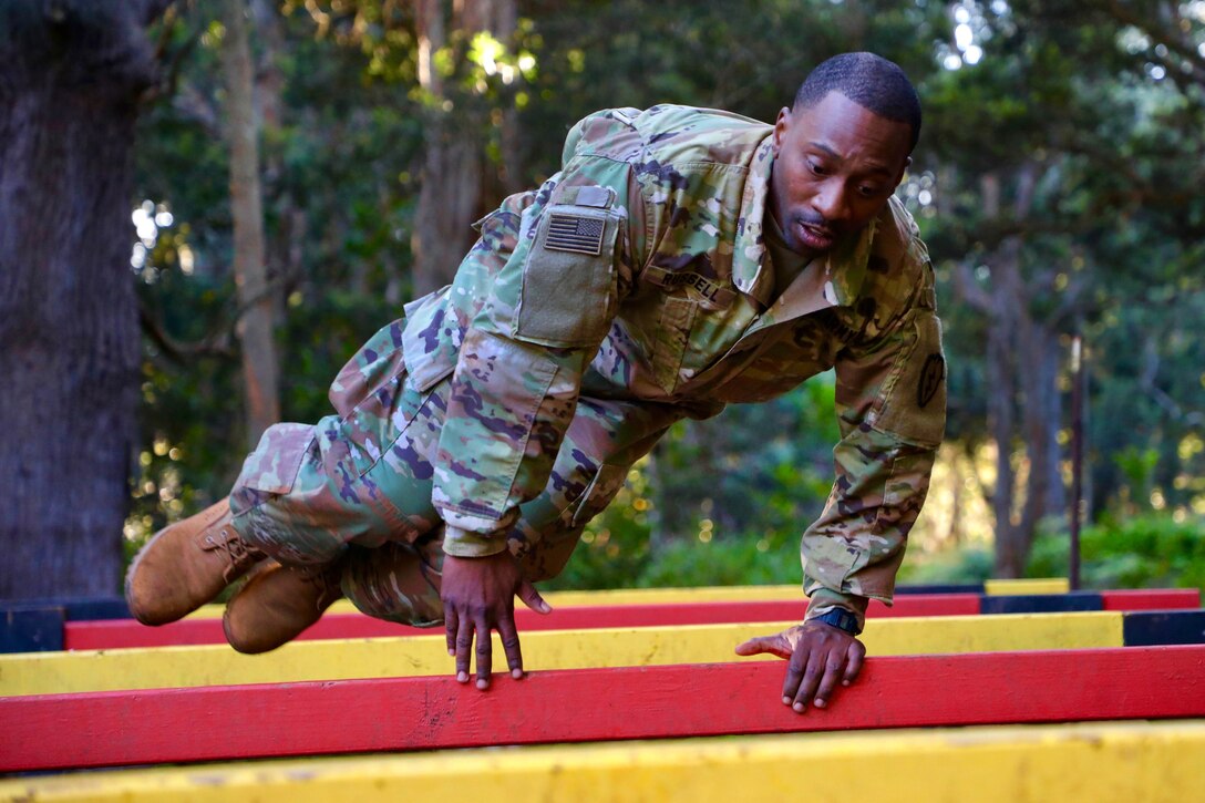 A soldier leaps over the high hurdle obstacle.