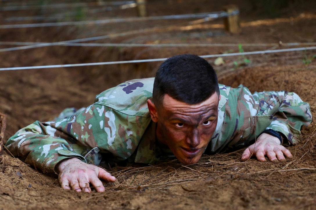 A soldier low crawls under a wire obstacle.