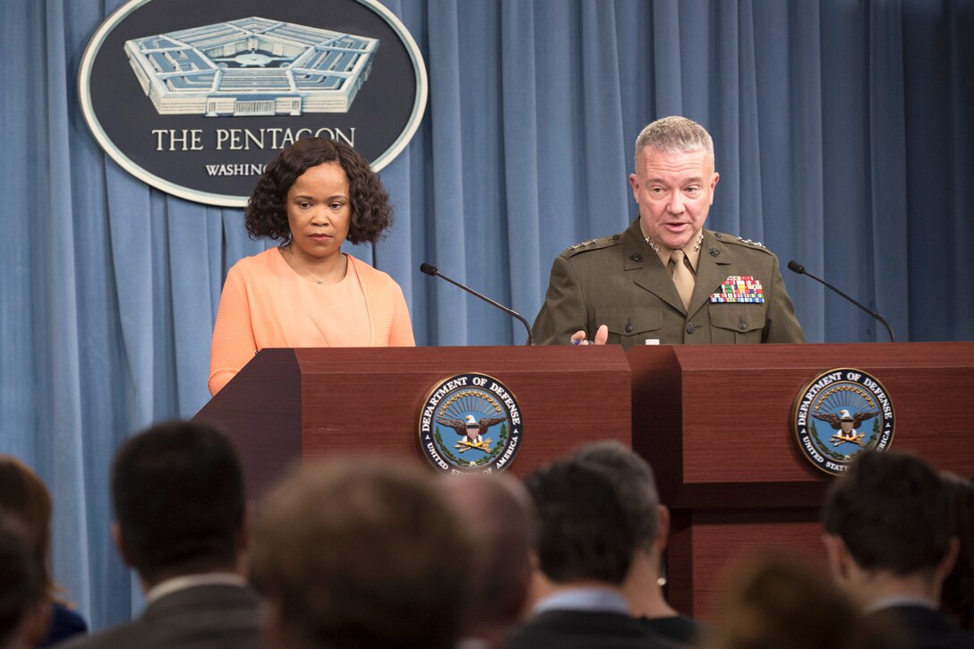 A civilian and a Marine general stand behind a podium.