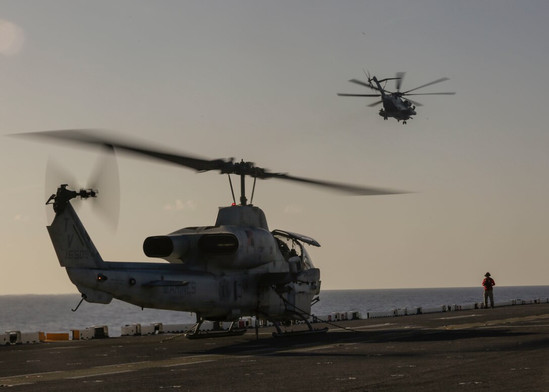 A CH-53E Super Stallion flies over an idling AH-1W Super Cobra, both with 2nd Marine Aircraft Wing, on the deck of the USS Kearsarge, April 18, 2018. The aircraft arrive in support of Navy Week New Orleans, providing the opportunity for the public to learn about interoperability between the Marine Corps and Navy.