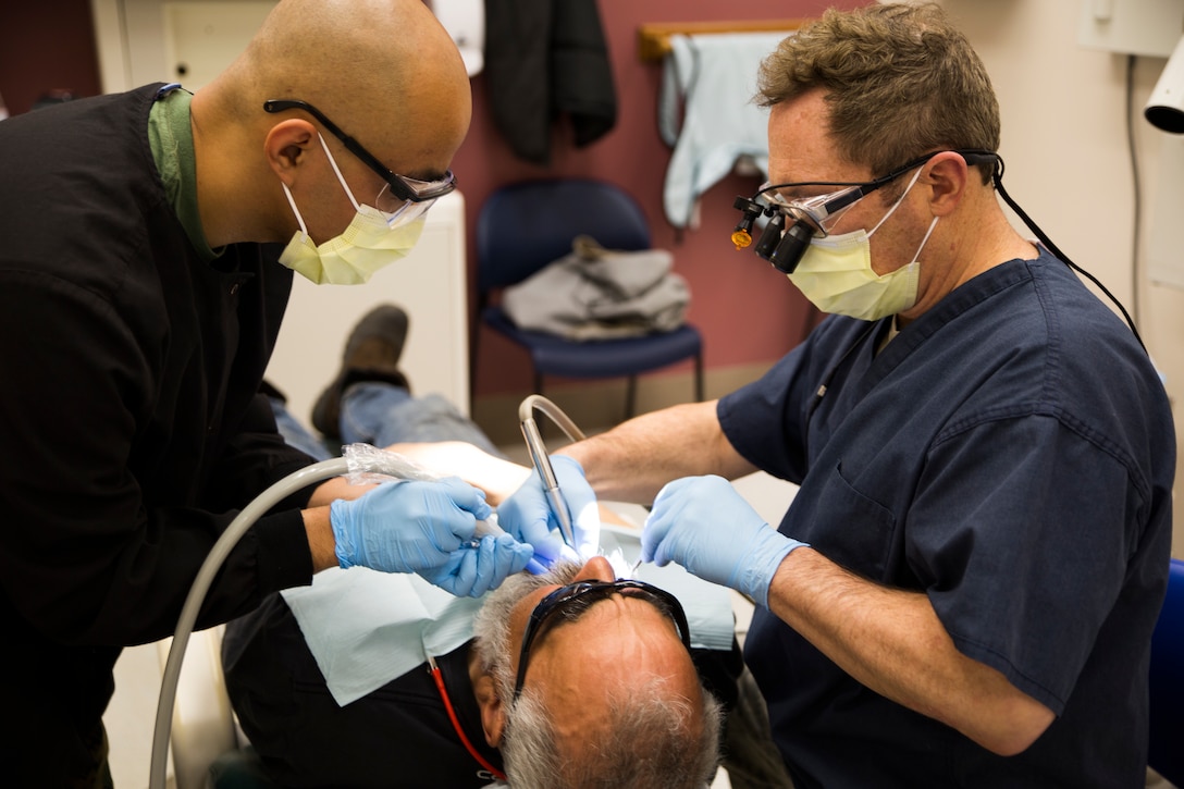 Navy Petty Officer 2nd Class Adrian B. Echevarri, left, dental leading petty officer with 4th Dental Battalion, 4th Marine Logistics Group, assists Air Force Col. Clifford Zdanowicz, right, a dental officer with 512 Aerospace Medicine Squadron, with a dental procedure on a local citizen during Innovative Readiness Training Arctic Care 2018, Kotzebue, Alaska, April 19, 2018.