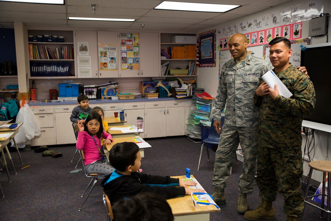 Air Force Maj. Courtland Pitt, left, a Chaplin with 110th Medical Group, introduces Marine Corps Cpl. Chandarong Ouk, right, an embarkation specialist with 4th Medical Battalion, 4th Marine Logistics Group, to a classroom of students during a career day at the Kotzebue Elementary School, Kotzebue, Alaska, April 19, 2018.