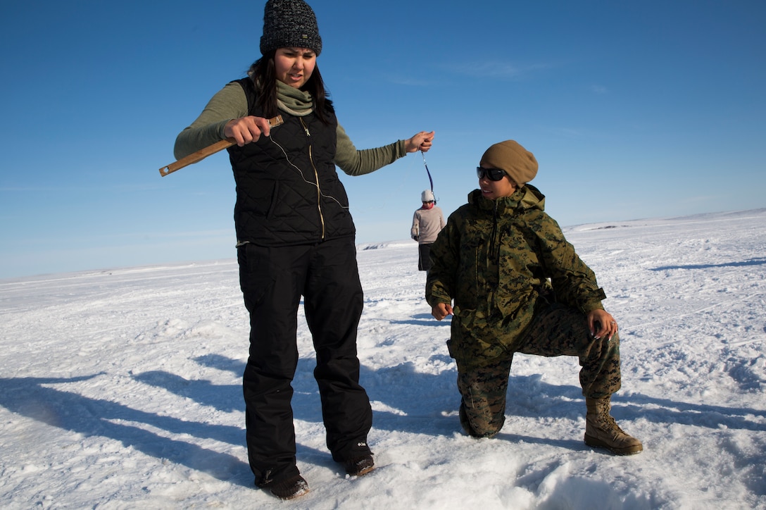 Marine Corps Sgt. Veronica J. Rios, right, an embarkation specialist with 4th Medical Battalion, 4th Marine Logistics Group, learns how to ice fish on the Kotzebue Sound from Puyuk Joule, a local member of the community during Innovative Readiness Training Arctic Care 2018, Kotzebue, Alaska, April 19, 2018.