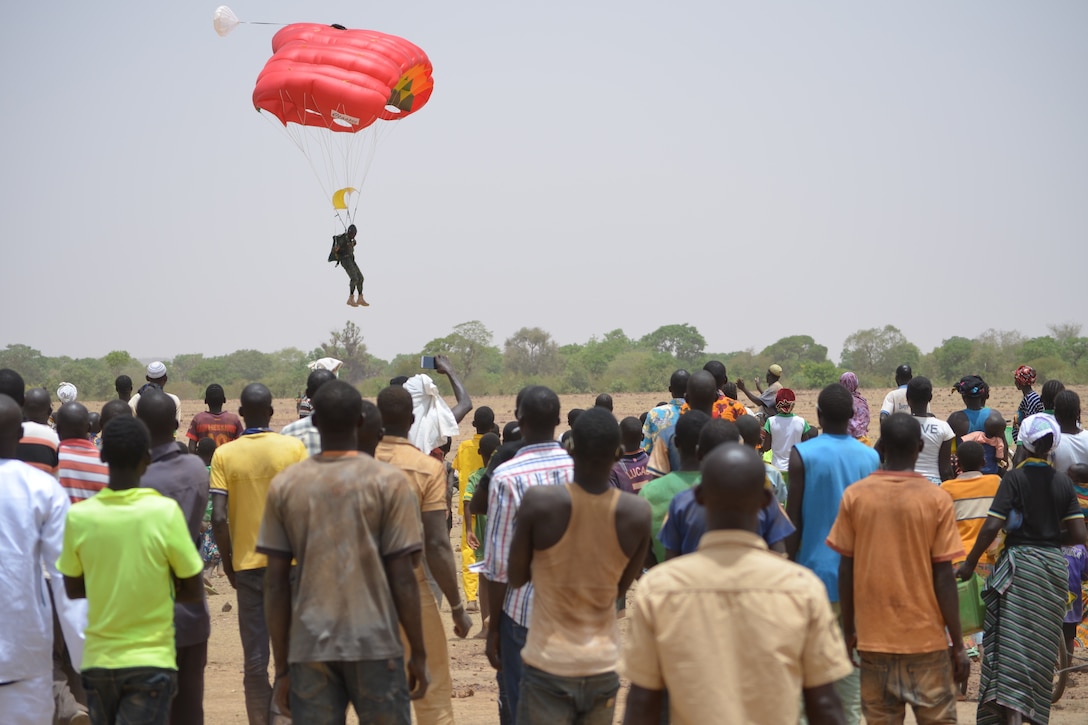 Villagers watch as a man parachutes to the ground.