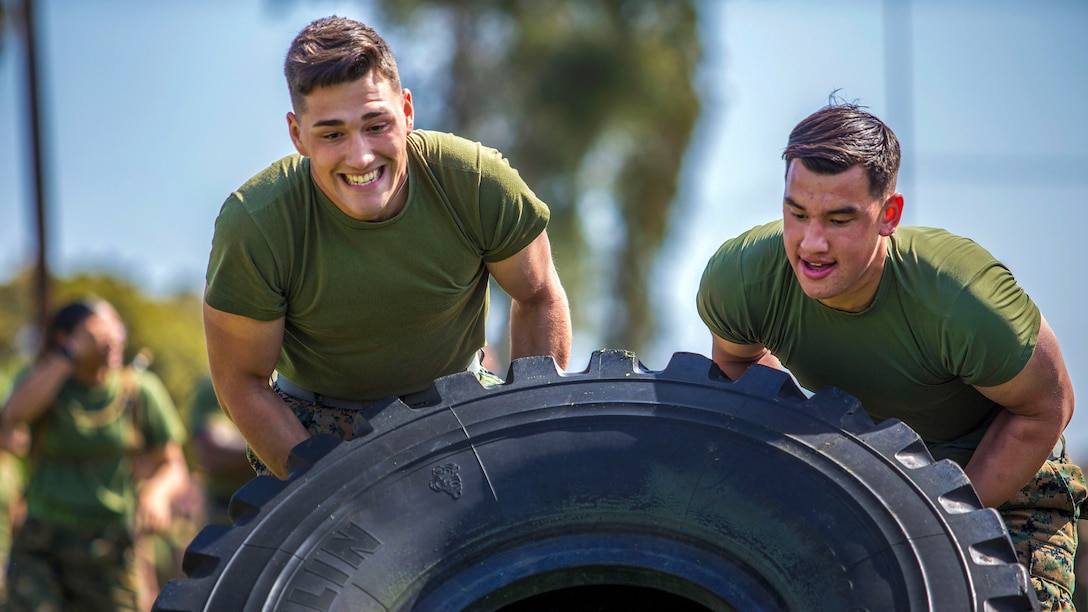 Two Marines push a tire in an effort to flip it.