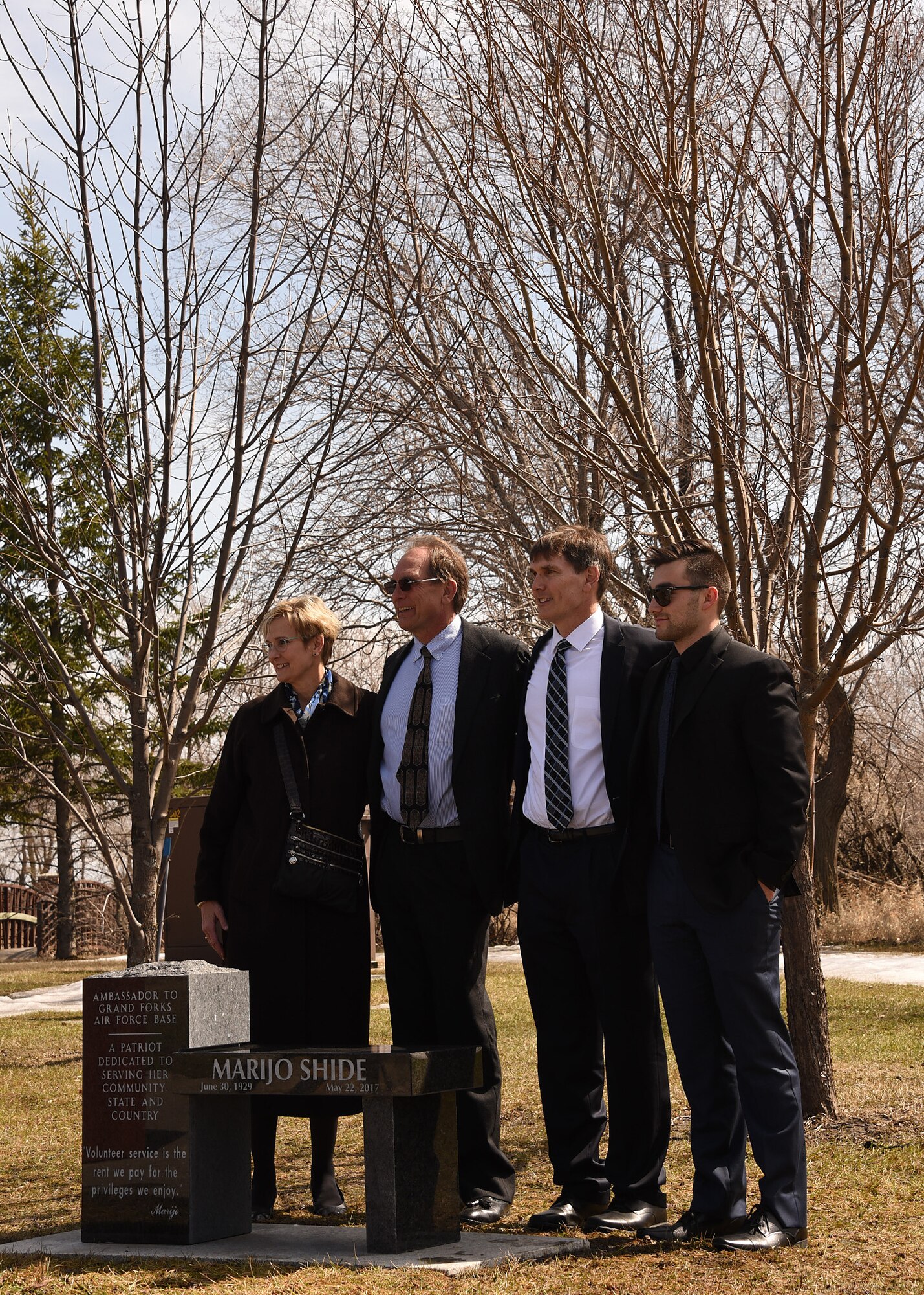 Members of Marijo Shide’s family pose for a photo behind a memorial in her honor, following the ceremony attended by more than 50 Airmen, ambassadors, friends and family members April 20, 2018, on Grand Forks Air Force Base, N.D. The dedicated bench stands near the Prisoners of War and Missing in Action Memorial Park, near the front gate of the base, and is open to the public. (Air Force photo by Airman 1st Class Elora J. Martinez)