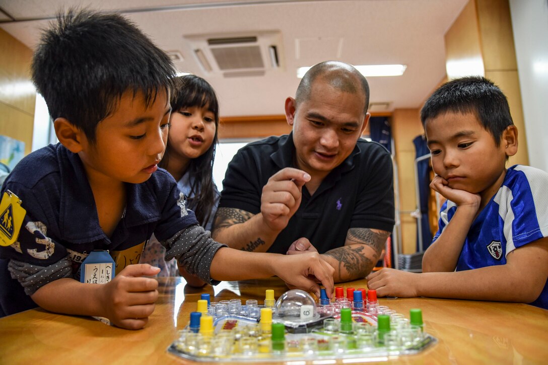 A sailor plays a board game with children sitting at a table.