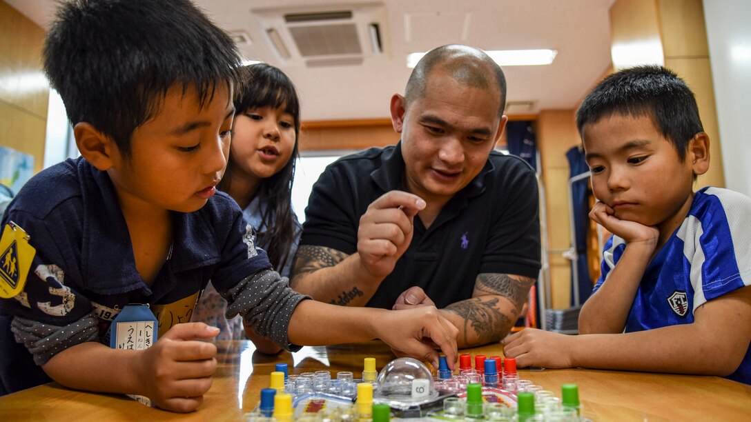 A sailor plays a board game with children sitting at a table.