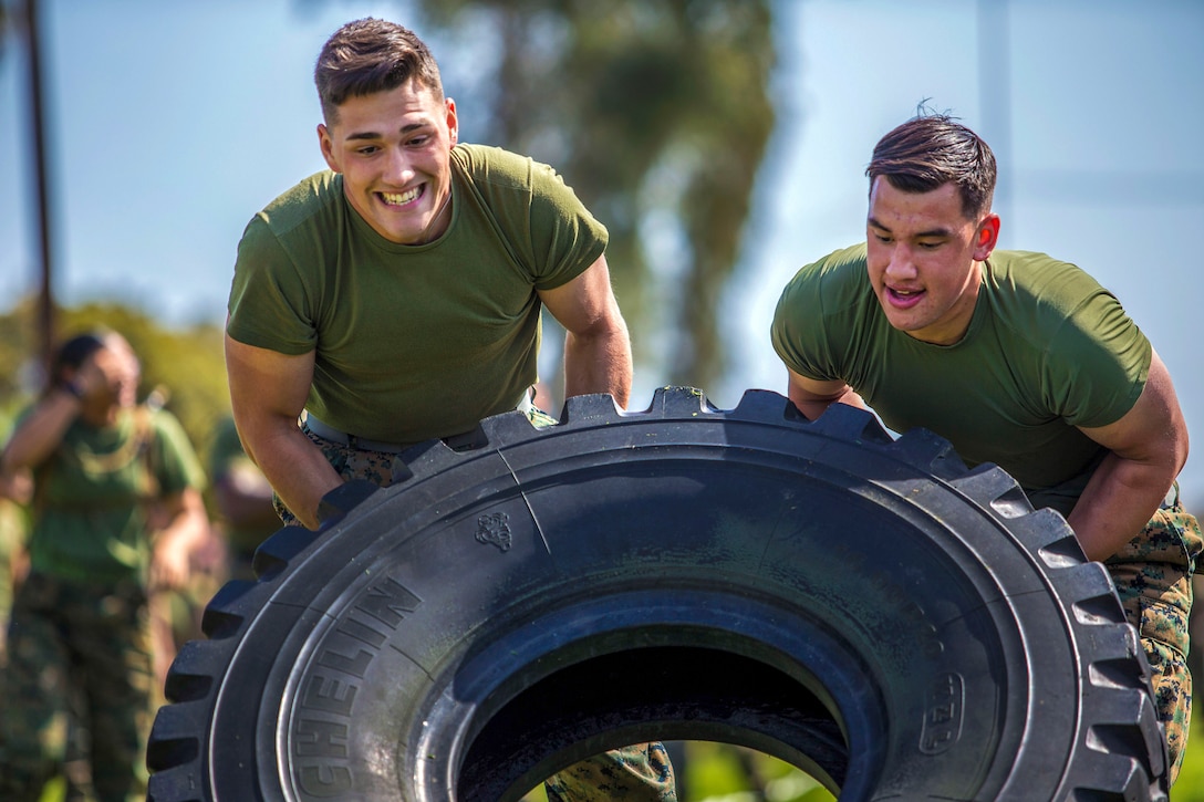 Two Marines push a tire in an effort to flip it.