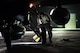 an airman places a yellow tire chalk behind the back wheel of an f-16 fighting falcon at night
