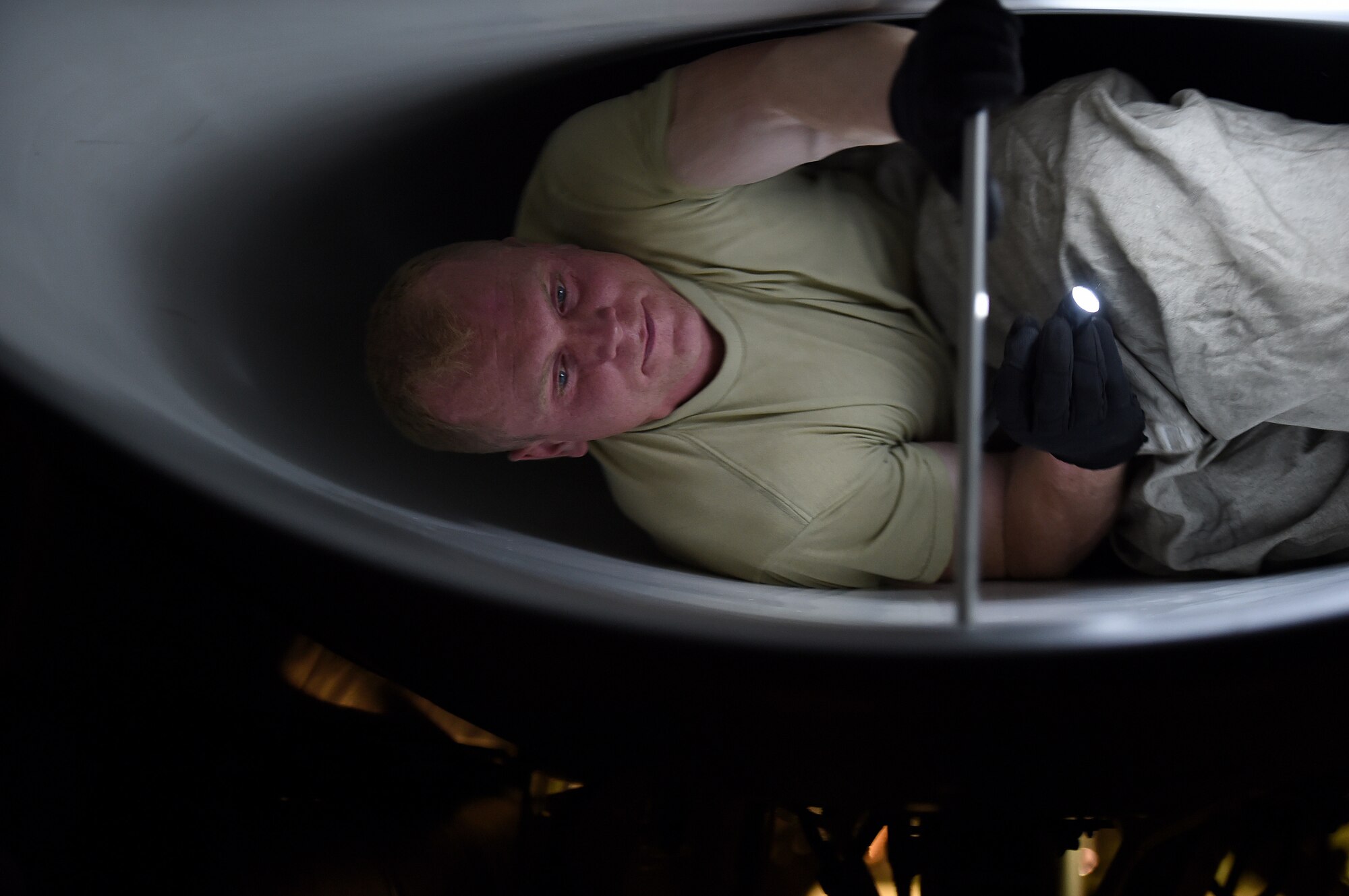 An Airman crawls out of a dark tiny f-16 engine intake