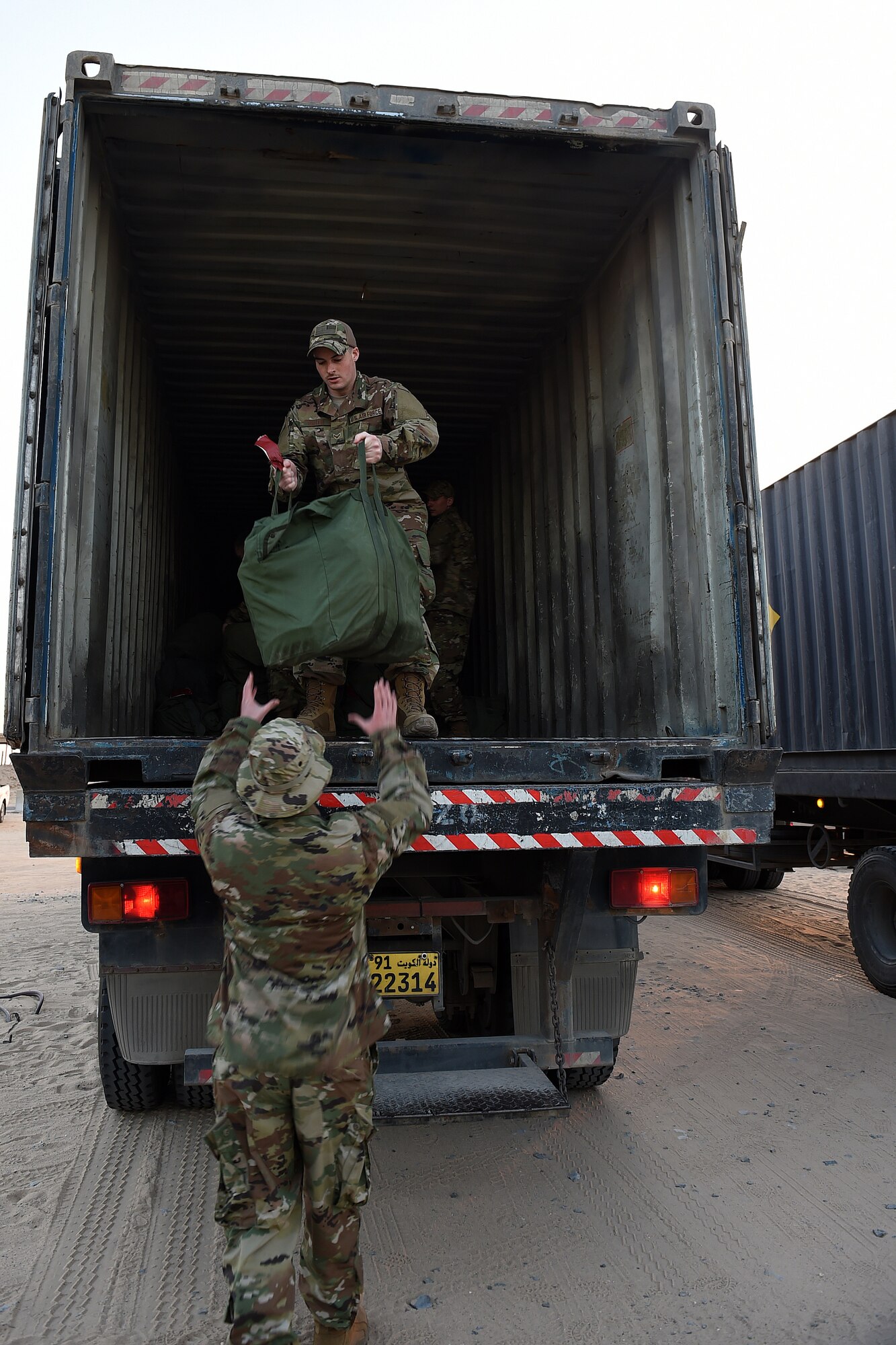 An airman inside a large truck hands a green mobility bag to another airman on the ground