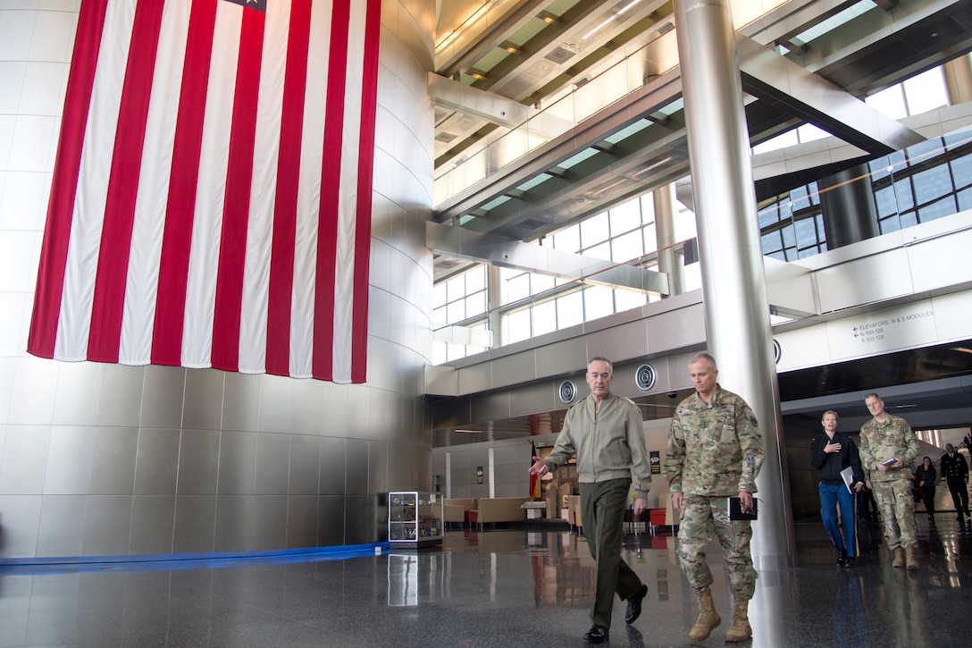 The chairman of the Joint Chiefs of Staff walks with an Army lieutenant general in a building lobby.