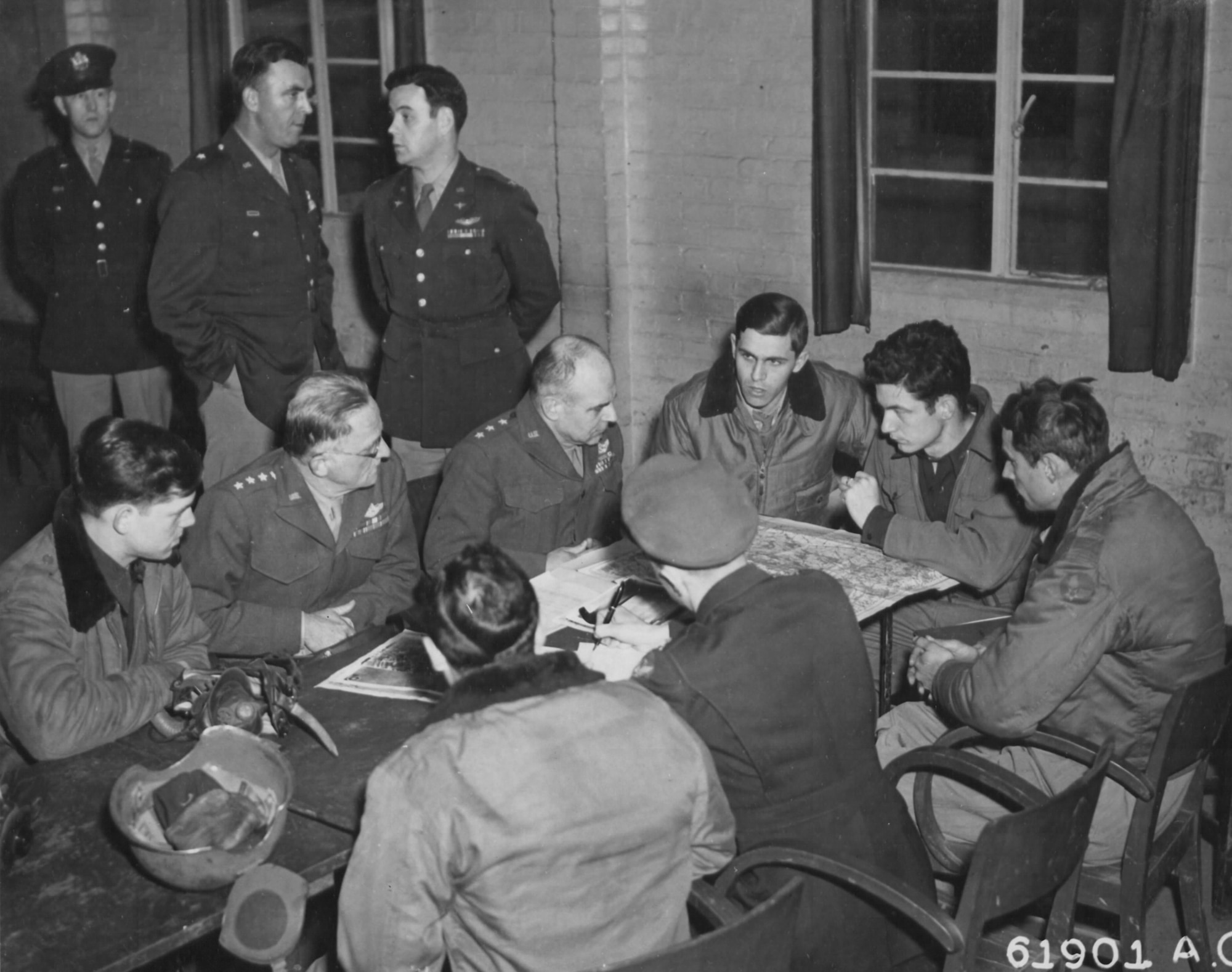 Gen Spaatz (2nd from left) and Lt Gen Doolittle (3rd from left) discuss results of a bombing attack with Eighth Air Force Airmen who just returned from the mission (note armored helmet and oxygen mask on the table).