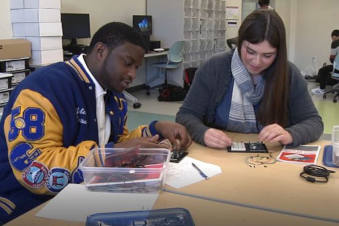 Two students sit at a table and work on a project.