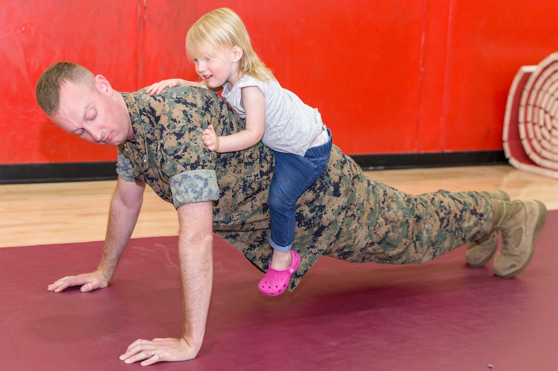Captain Kendall Ignatz decides that normal push-ups are not enough and allows his daughter to sit on his back to create more resistance during the Big Marine Little Marine High Intensity Tactical Training (HITT), held in the Semper Fit gym, aboard Marine Corps Logistics Base Barstow, Calif., April 18.