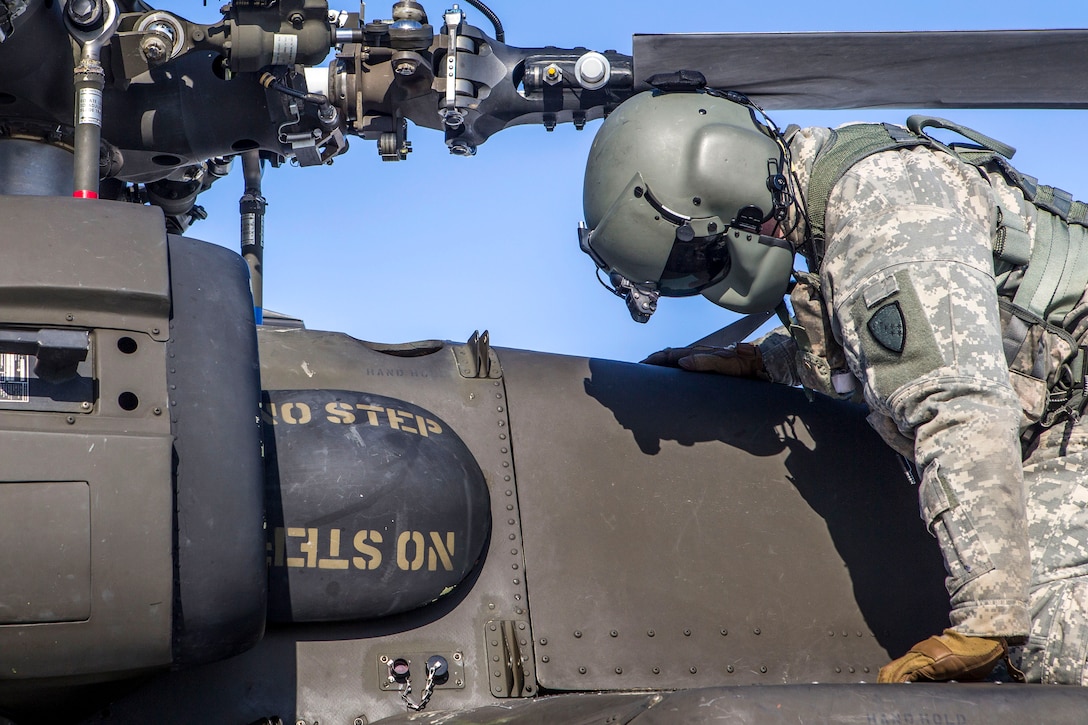 An Army crew chief performs checks on a helicopter’s main rotor blades.
