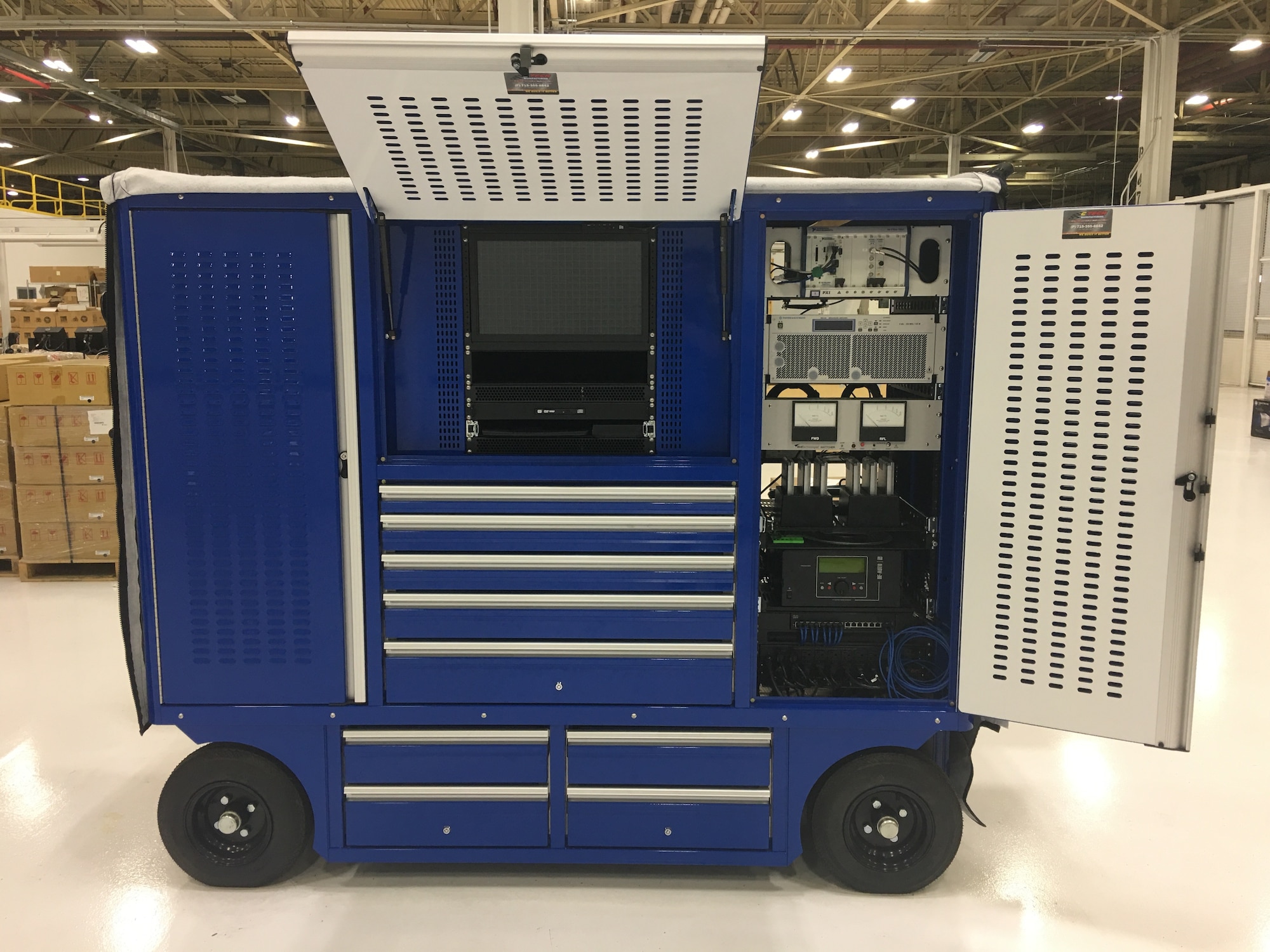 A pit box during operation. The equipment on the right is the operational equipment used to energize the E-3 aircraft for testing. The middle bay shows a monitor and keyboard the operators use to monitor and operate the system. An identical set of equipment is kept in the left bay, as requested by the customer. Should a piece fail and need to be replaced, this provides them a replacement part for immediate replacement.