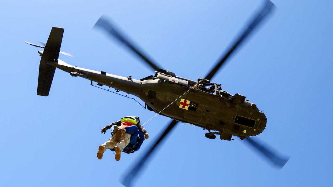 A helicopter, shown from overhead, hoists two service members dangling from a line.