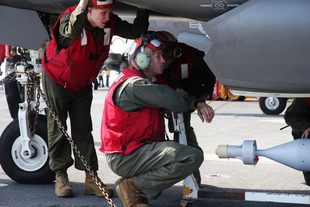 A Marine supervises a bomb being loaded onto an aircraft.