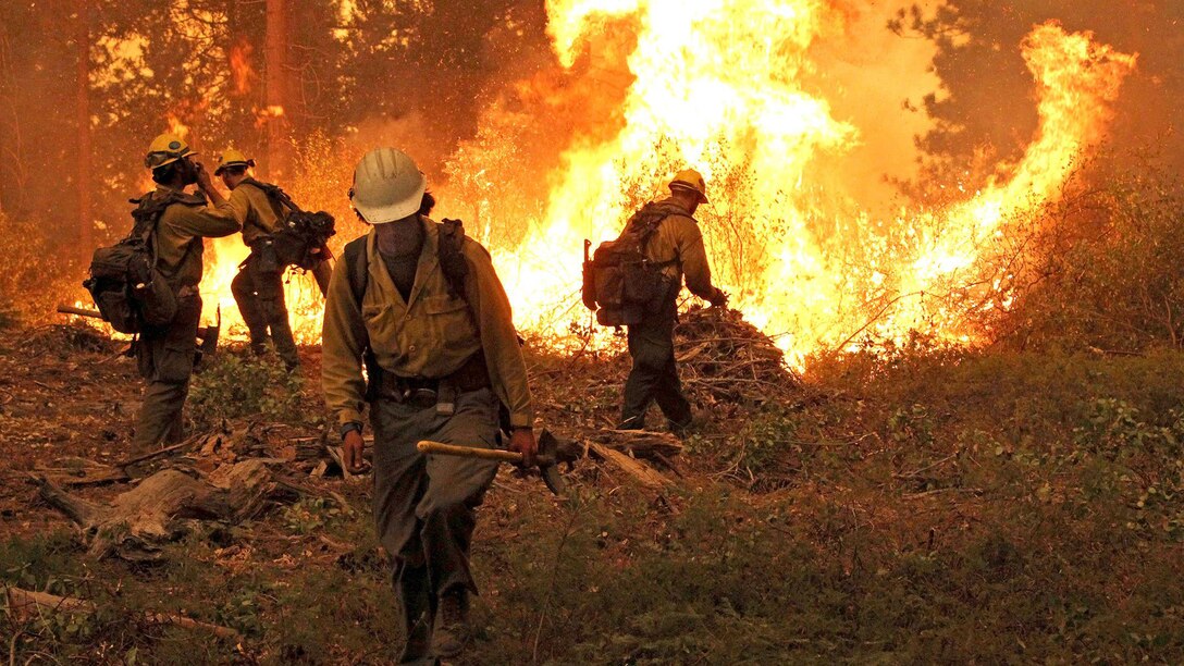 Firefighters in the foreground are combating a fire in the background