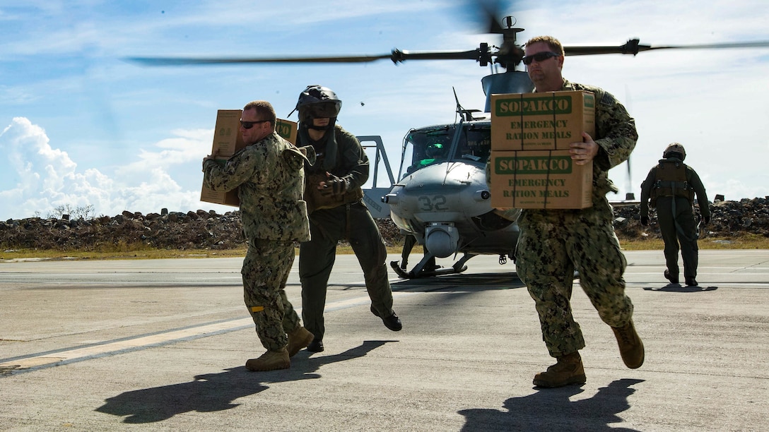 Service members carry relief supply boxes from a helicopter