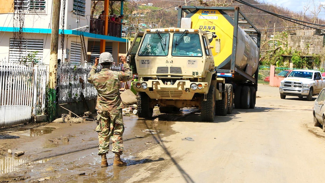 A Puerto Rico Army National Guardsman directs a truck transporting water down a street in Puerto Rico