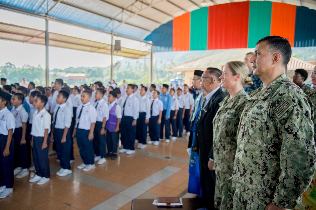 Sailors stand while students sing the Malaysian national anthem.
