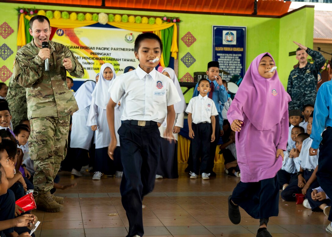 A soldier cheers on students during a relay race.