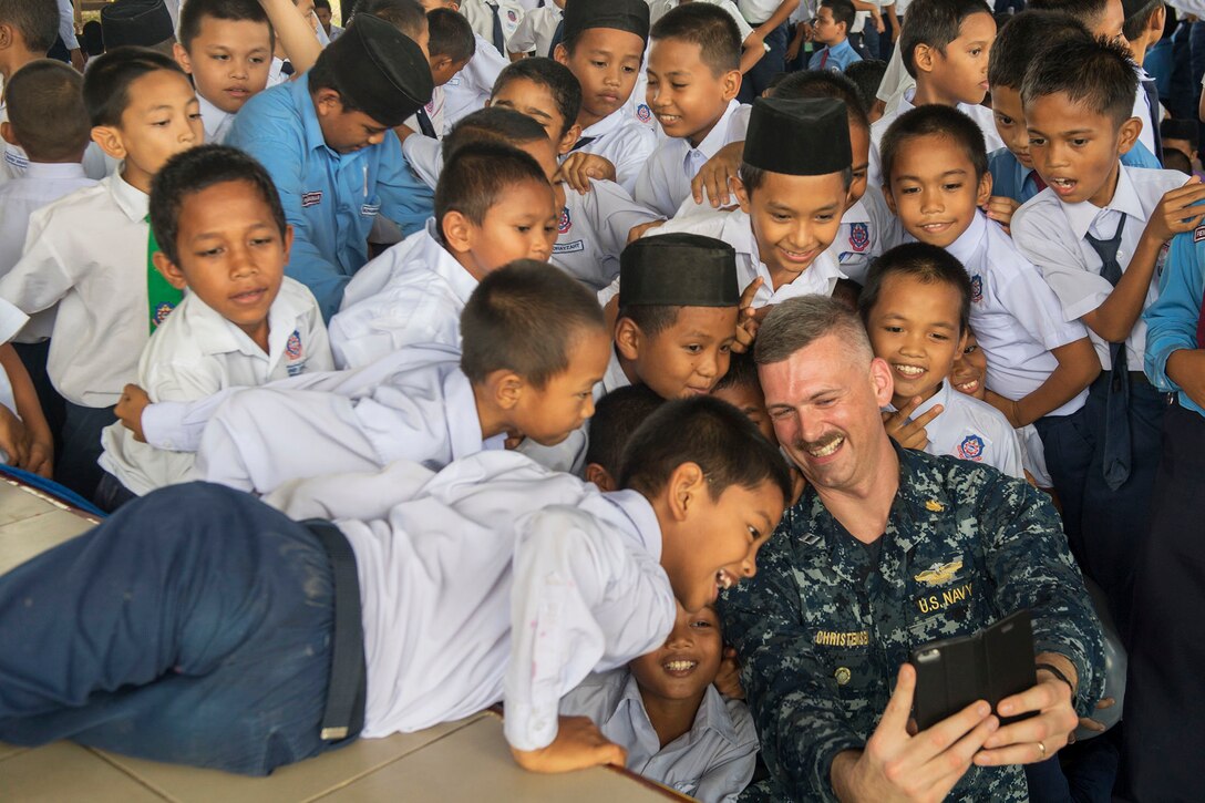 A sailor takes a selfie with students.