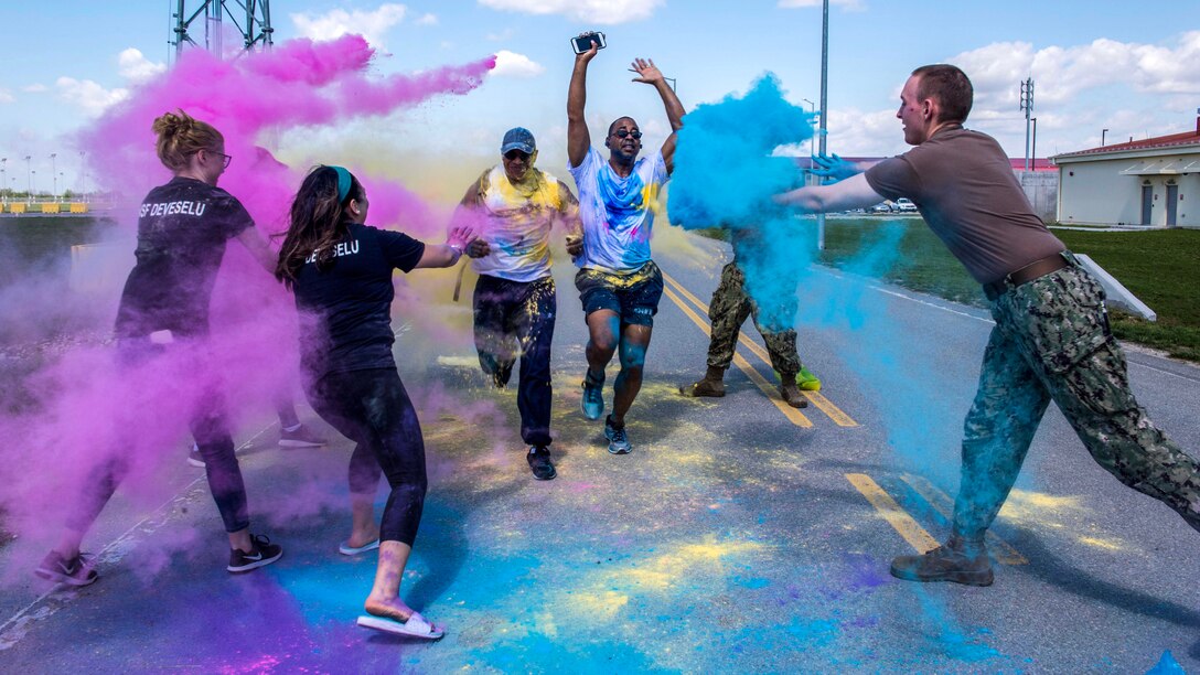 Sailors throw turquoise and mauve powder on a pair of runners on a road.