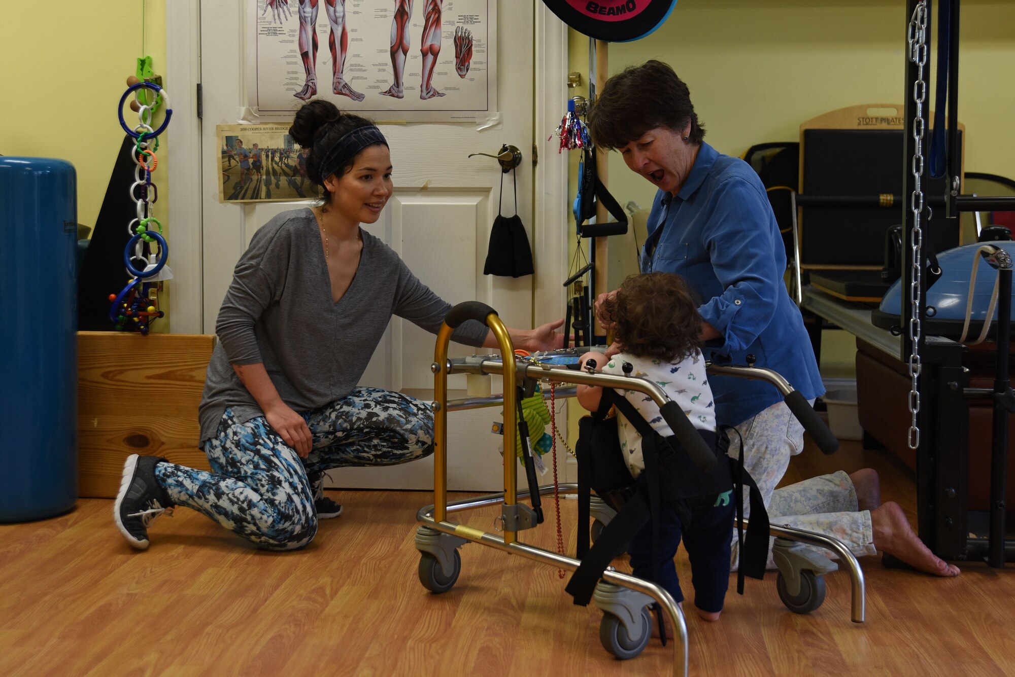 Ashley Mockovciak, Team Shaw spouse, left, rings a bell to attract the attention of her son, Noah Mockovciak, as Kathleen Ganley, physical therapist, guides his walker in a physical therapy office at Columbia, S.C., March 1, 2018.