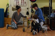 Ashley Mockovciak, Team Shaw spouse, left, rings a bell to attract the attention of her son, Noah Mockovciak, as Kathleen Ganley, physical therapist, guides his walker in a physical therapy office at Columbia, S.C., March 1, 2018.