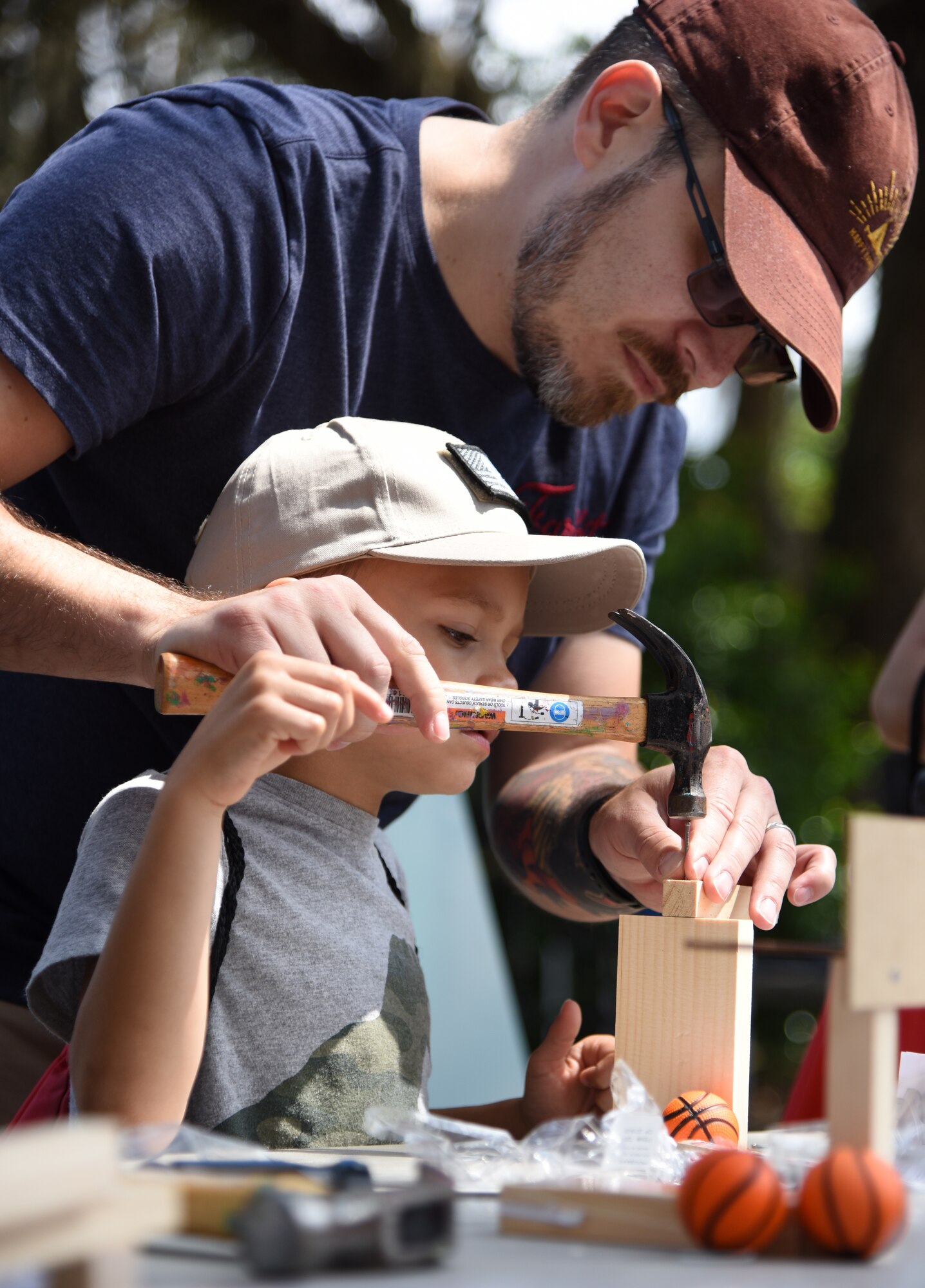 Austin Herrera and his son, Nolan, assemble a miniature wooden basketball court during Child Pride Day at Marina Park at Keesler Air Force Base, Mississippi, April 21, 2018. Games, fun runs, pontoon boat rides and educational displays were available for military families who attended. (U.S. Air Force photo by Kemberly Groue)