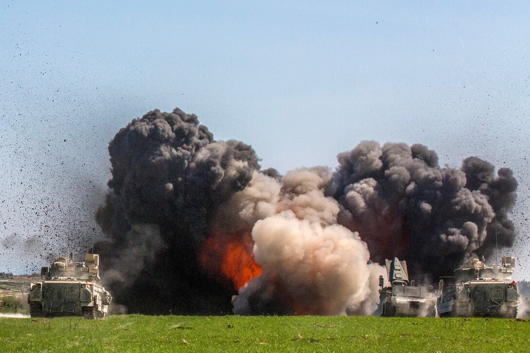 Black clouds of smoke and flames fill the air in a field, as tanks conduct training.