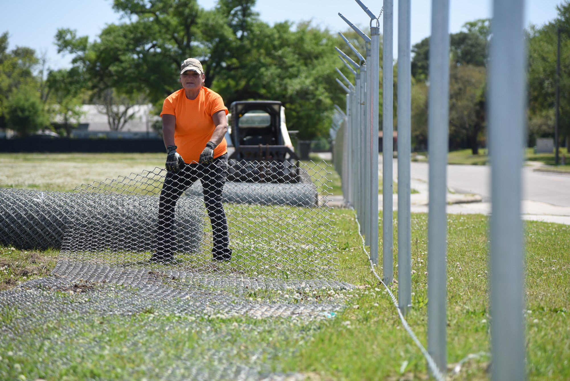 Jewell Gonzalez, Gulf Coast Fence Company laborer, unrolls fencing in the open grass area near the commissary at Keesler Air Force Base, Mississippi, April 10, 2018. The fence will serve as a perimeter around the site of the new Division Street Gate entrance construction. The estimated $37 million project will begin construction this summer. (U.S. Air Force photo by Kemberly Groue)