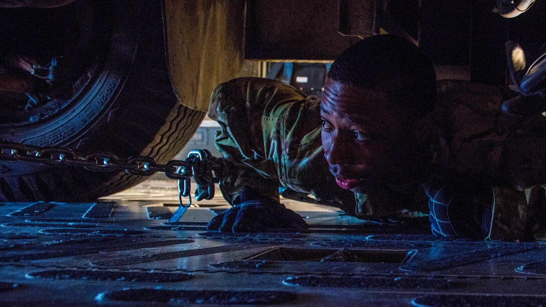 An airman lies on his stomach and looks at the undercarriage of a vehicle.