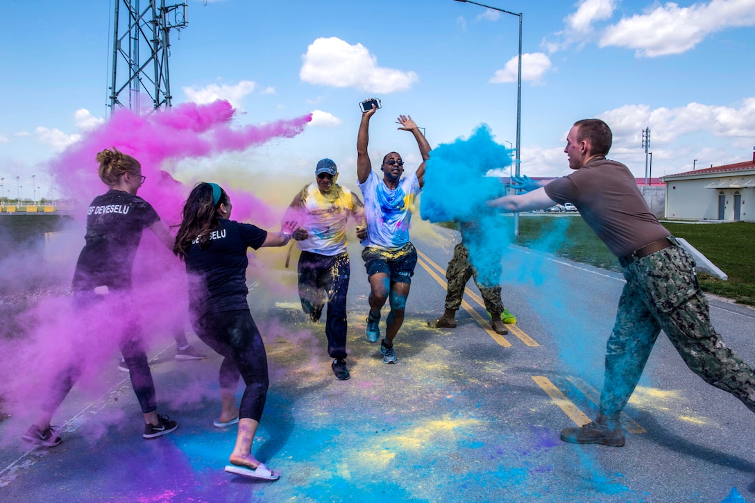 Sailors throw turquoise and mauve powder on a pair of runners on a road.