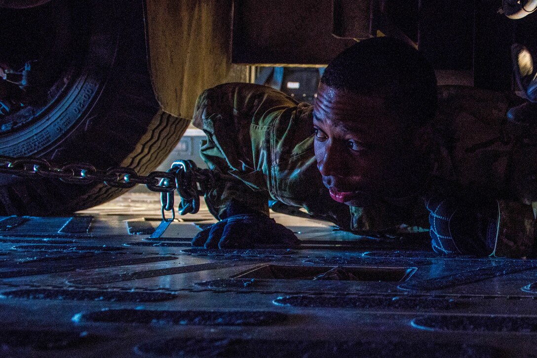 An airman lies on his stomach and looks at the undercarriage of a vehicle.