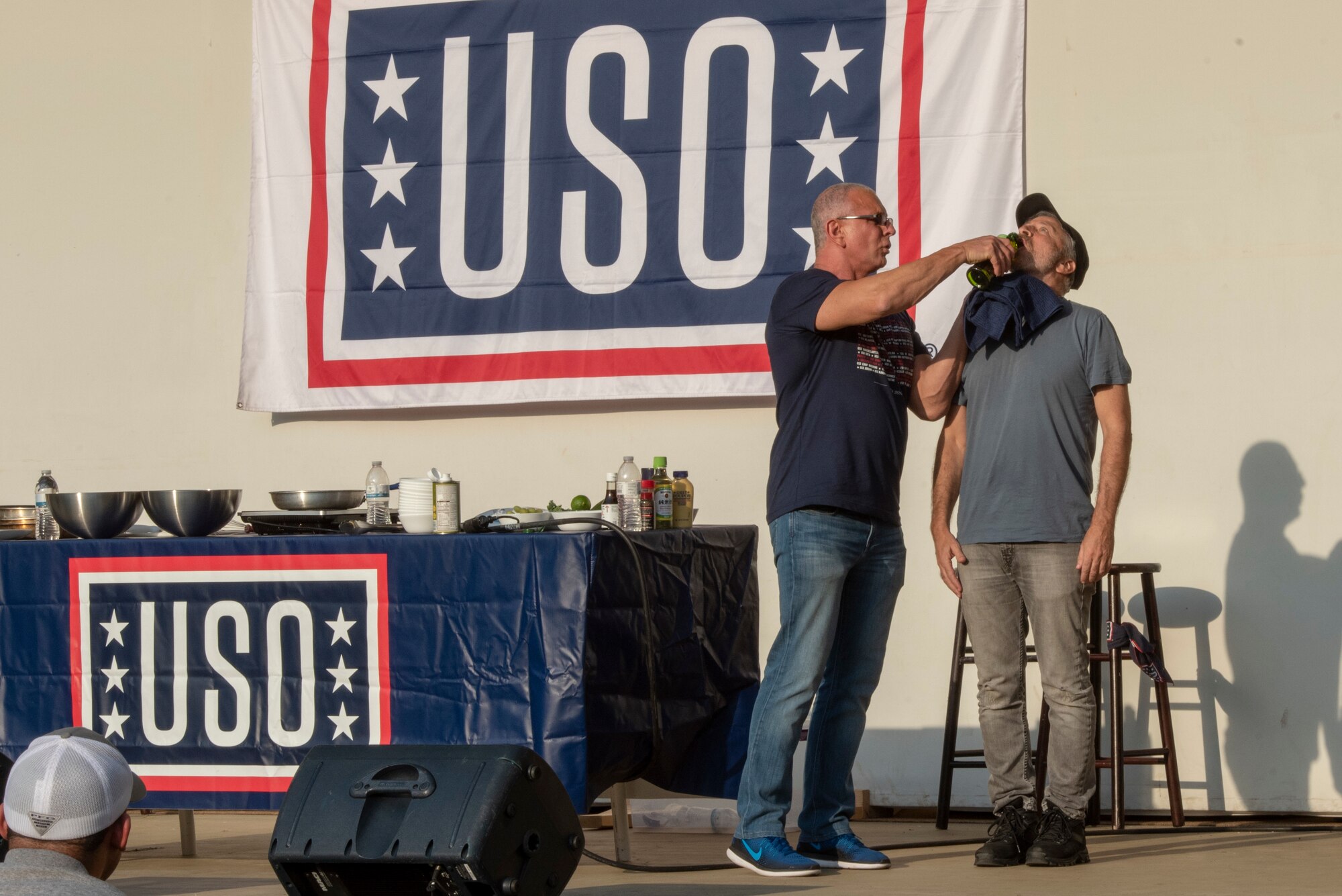 Robert Irvine, celebrity chef, feeds Jon Stewart olive oil as part of his cooking demonstration at the USO Spring Tour at Yokota Air Base, Japan, April 22, 2018.