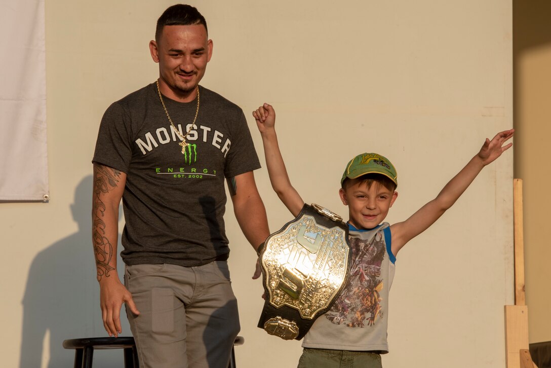 Max Holloway, UFC fighter and undisputed featherweight champion, allows a child from the audience to don his championship belt at the USO Spring Tour at Yokota Air Base, Japan, April 22, 2018.