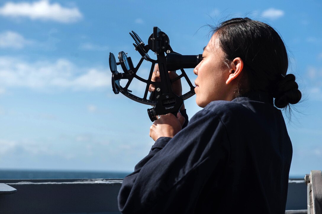 A sailor uses a sextant to help in navigating the USS Stockdale.