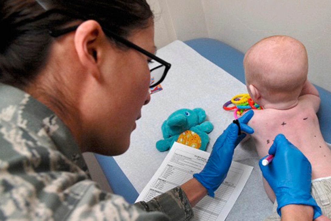 A military medical technician writes numbers on a baby's back.