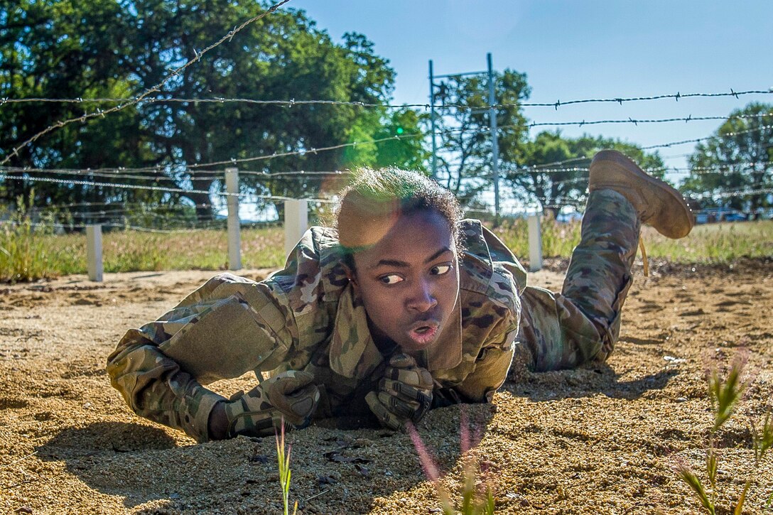 A soldier maneuvers under barbed wire.