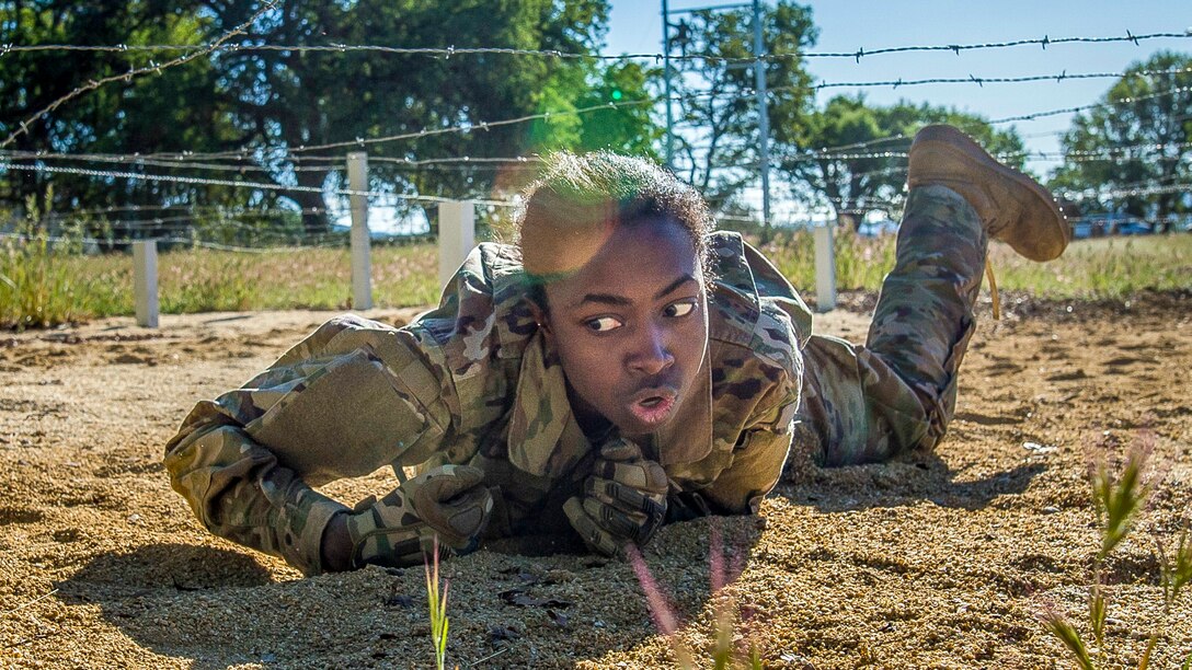 A soldier maneuvers under barbed wire.