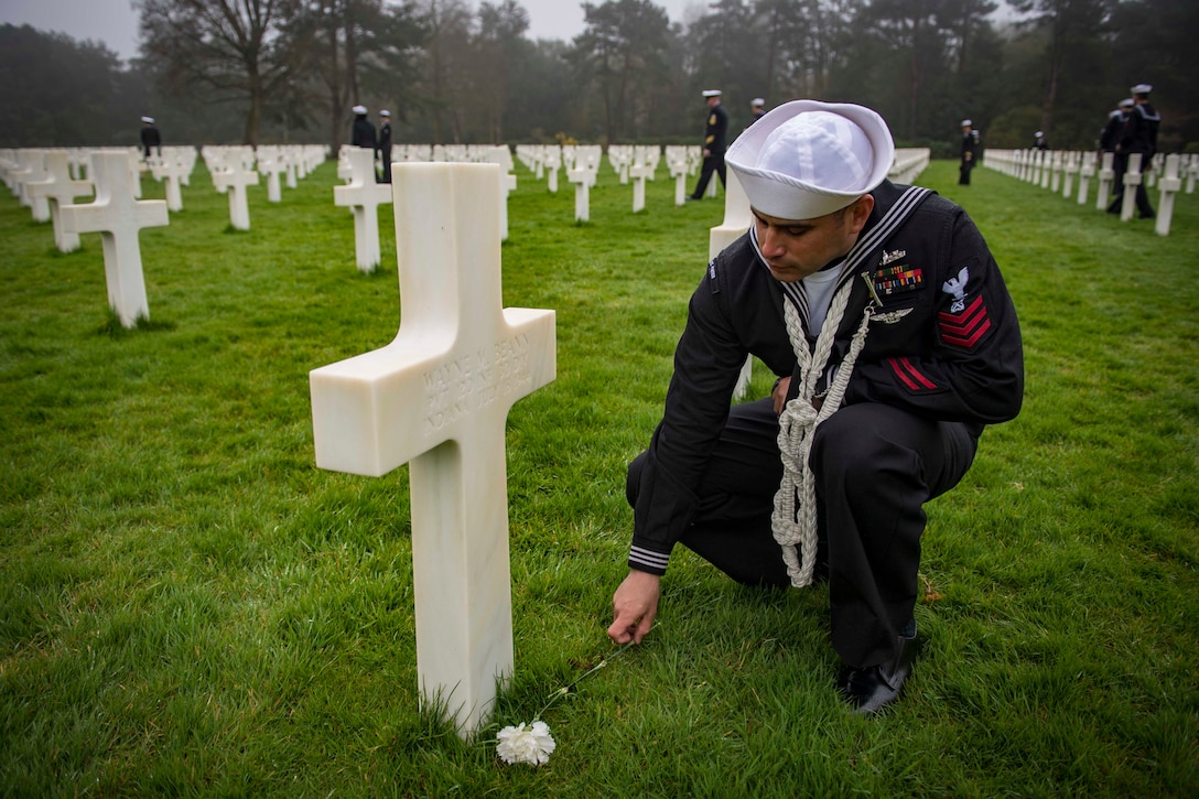 A sailor places a rose at a headstone at a cemetery in France.