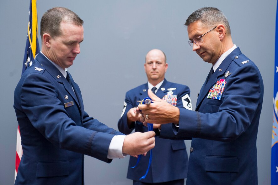 Col. Jonathan VanNoord (right), commander of the newly-activated 709th Surveillance and Analysis Group, slowly unfurls his group’s new guidon flag with the help of Col. Steven M. Gorski (left), commander of the Air Force Technical Applications Center, Patrick AFB, Fla.  VanNoord took command of the 709th SAG April 1, 2018.  Holding the guidon is Senior Master Sgt. Robert Christman, a squadron superintendent under VanNoord’s command.  (U.S. Air Force photo by Phillip C. Sunkel IV)